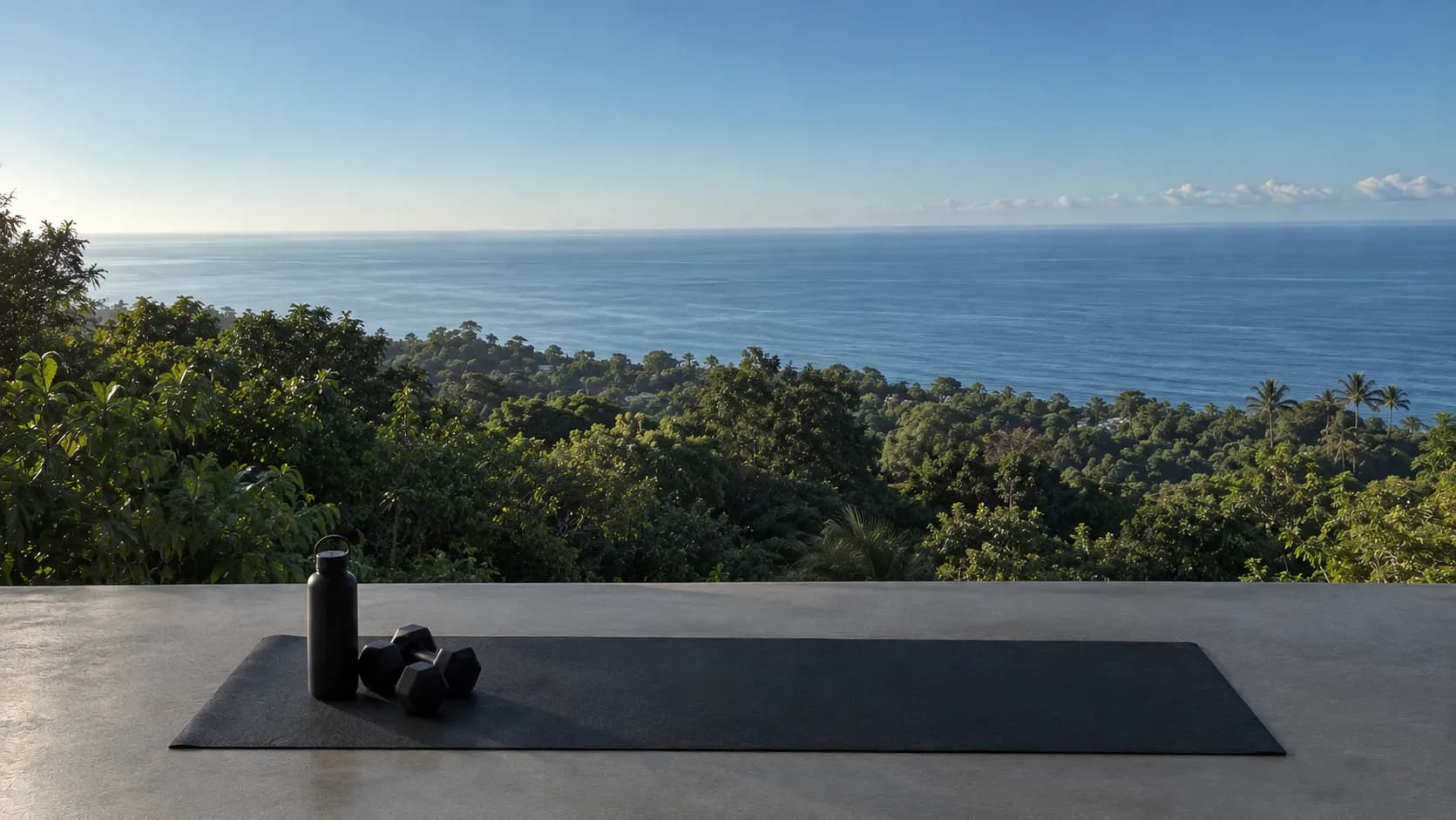 Yoga mat with a water bottle and dumbbells on a terrace above the rainforest and sea